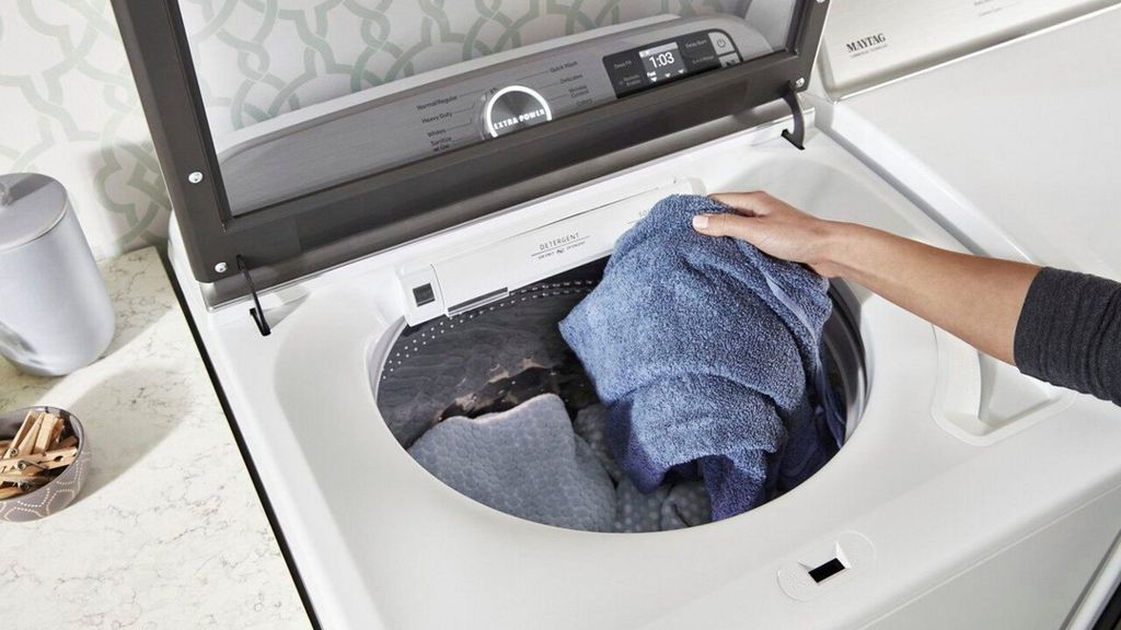 man putting laundry on top load washer