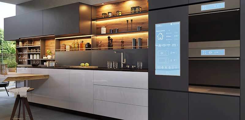 A modern kitchen with sleek gray cabinets and a built-in smart refrigerator with a digital display, highlighting the integration of IoT appliances into contemporary home design