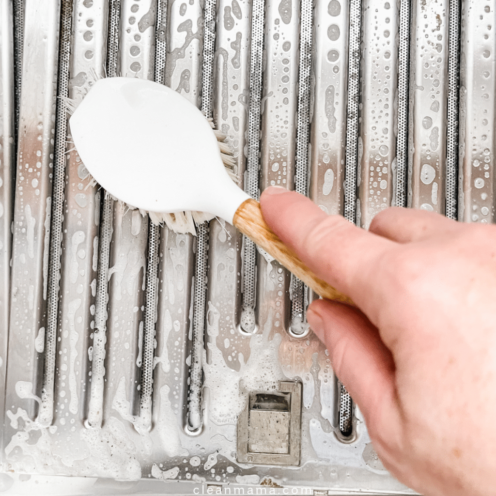 person cleaning a range hood filter with a brush