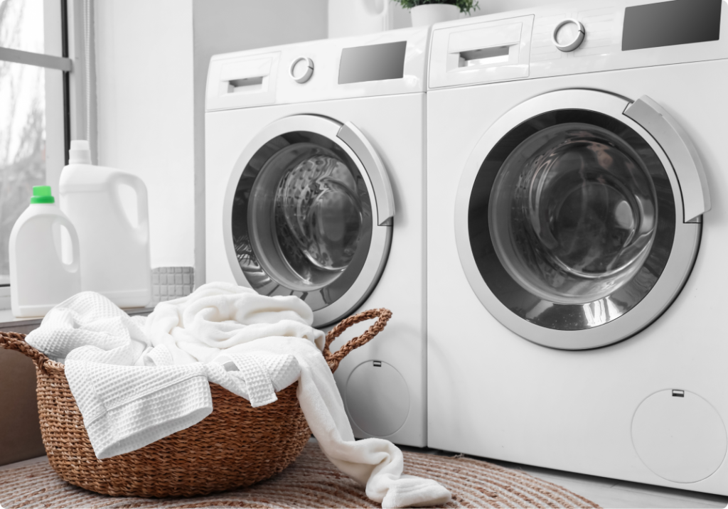 a laundry room with two front-loading washing machines and a laundry basket full of white clothes