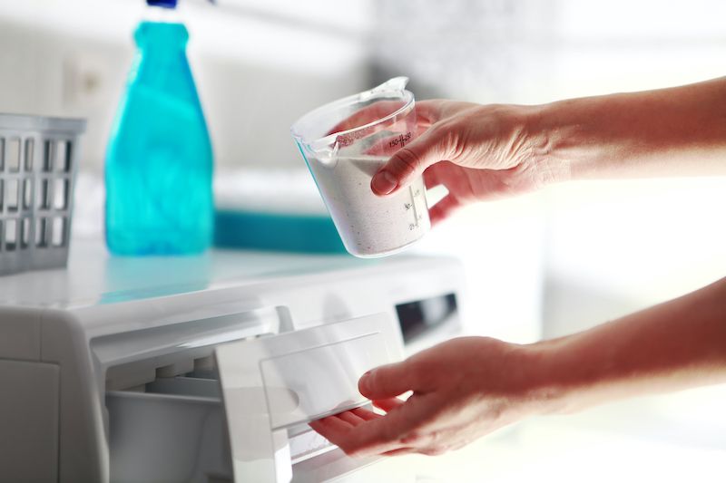 person adding powdered laundry detergent to a washing machine's dispenser drawer