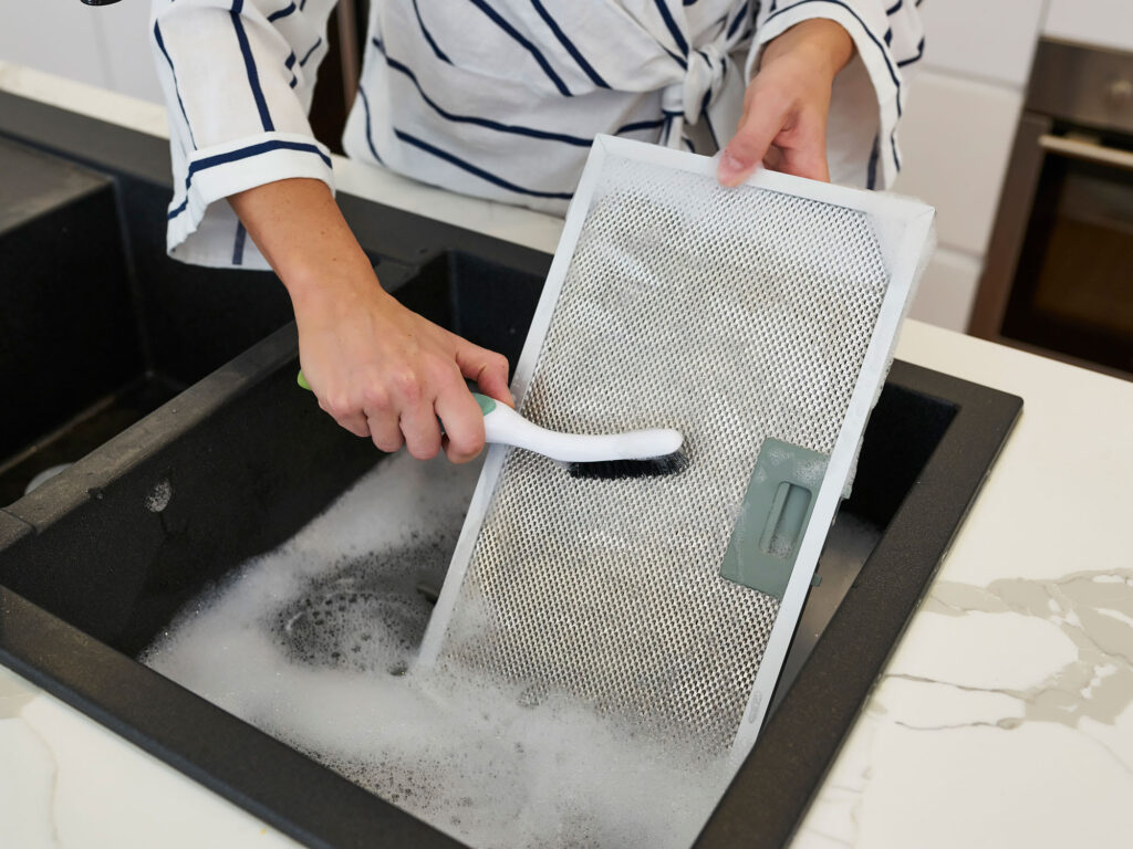 a person cleaning a range hood filter in a kitchen sink