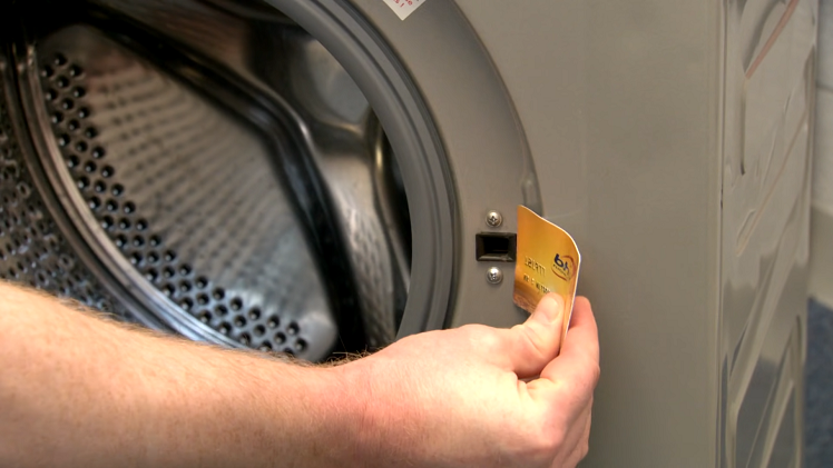 a person attempting to open a washing machine door using a credit card