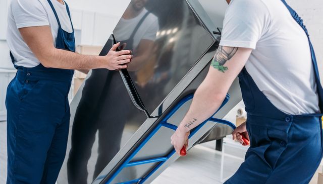two movers transporting a large appliance, likely a refrigerator, using a hand truck