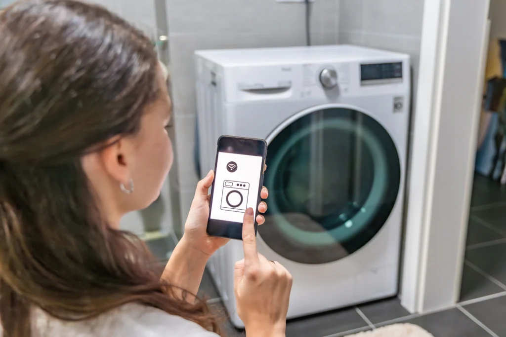a person using a smartphone app to remotely control a smart washing machine via Wi-Fi