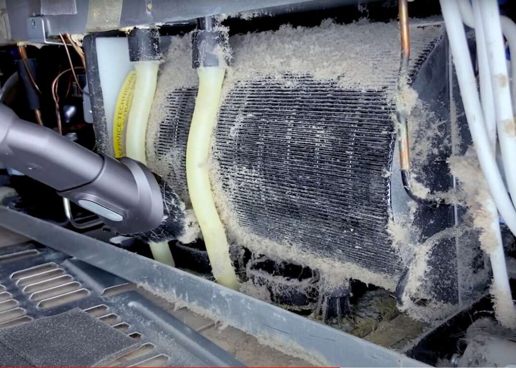 a refrigerator's condenser coils being cleaned with a vacuum cleaner