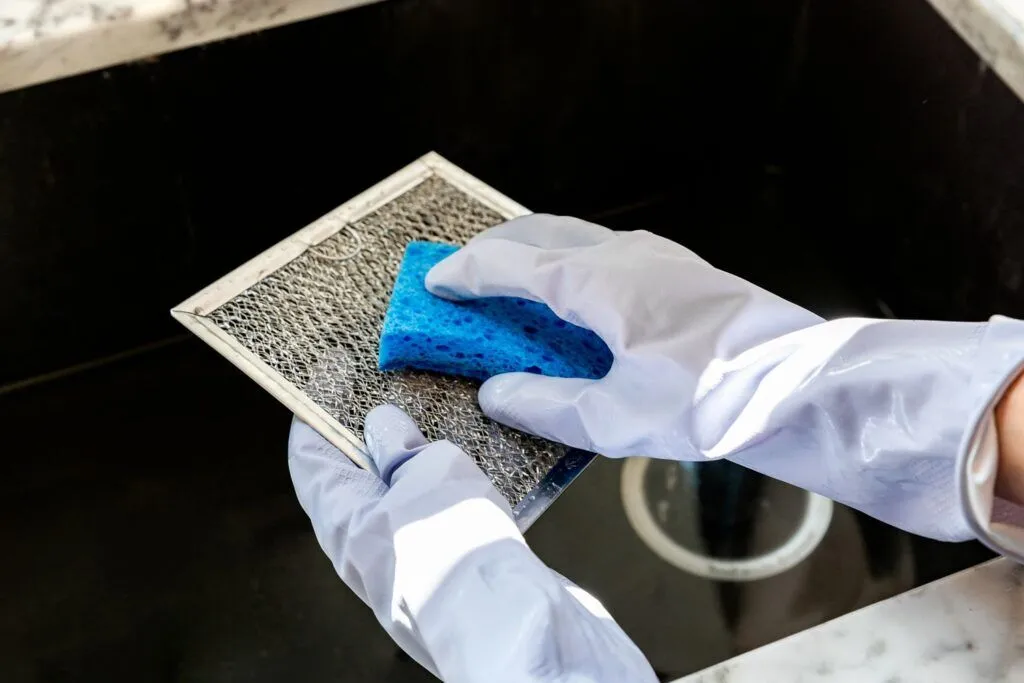 a person wearing white gloves and cleaning a metal mesh filter