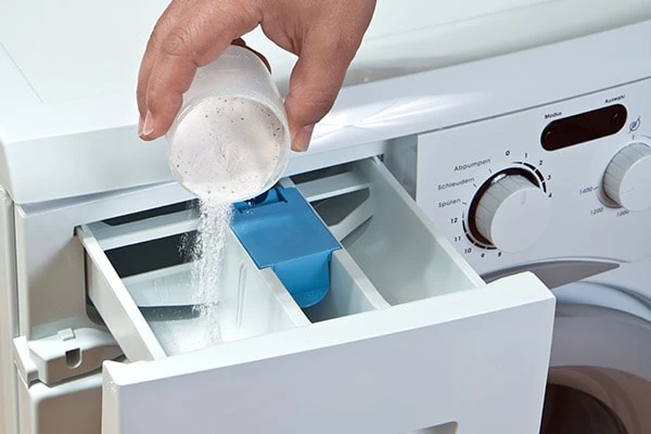 a person pouring powdered laundry detergent into a washing machine's dispenser drawer