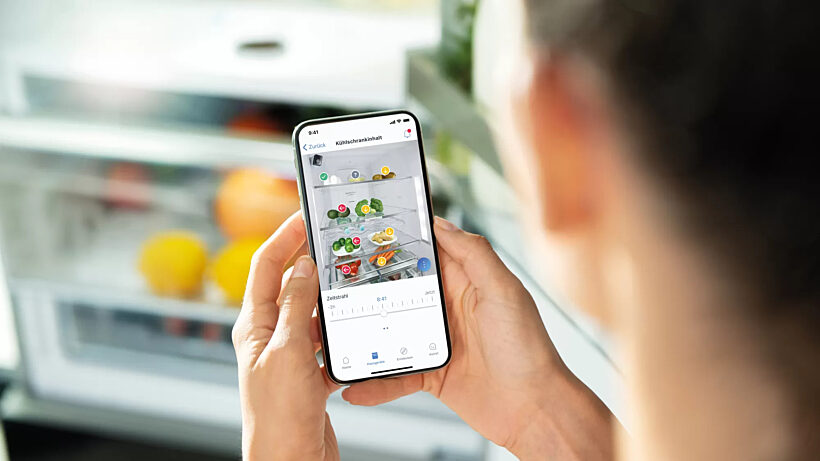 a person using the Home Connect app on a smartphone to view the inside of a smart refrigerator