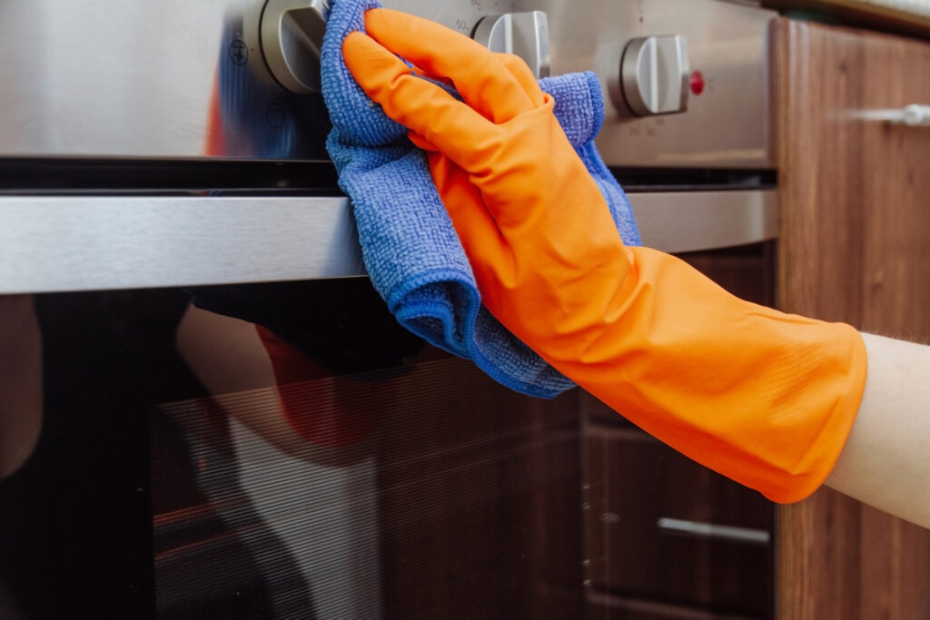 a person wearing orange gloves and using a blue microfiber cloth to clean the exterior of a stainless steel oven