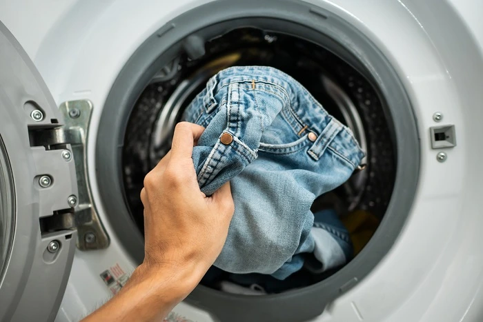 a person putting a pair of blue jeans into a front-load washing machine