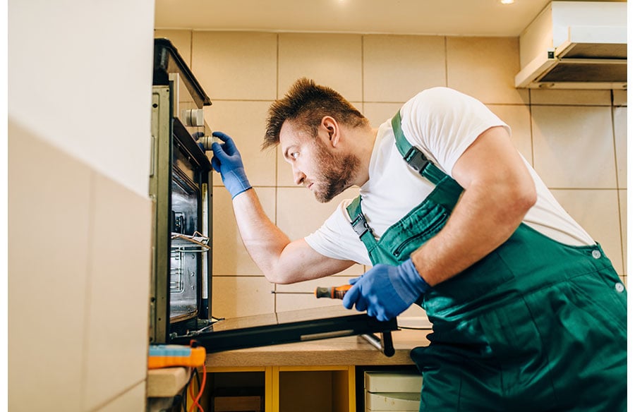 a professional worker, likely a technician or repairman, servicing an oven in a kitchen setting