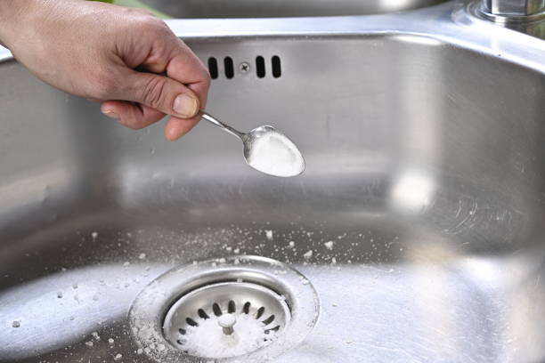 Cleaning kitchen sink with baking soda to keep sinks draining well and prevent clogs