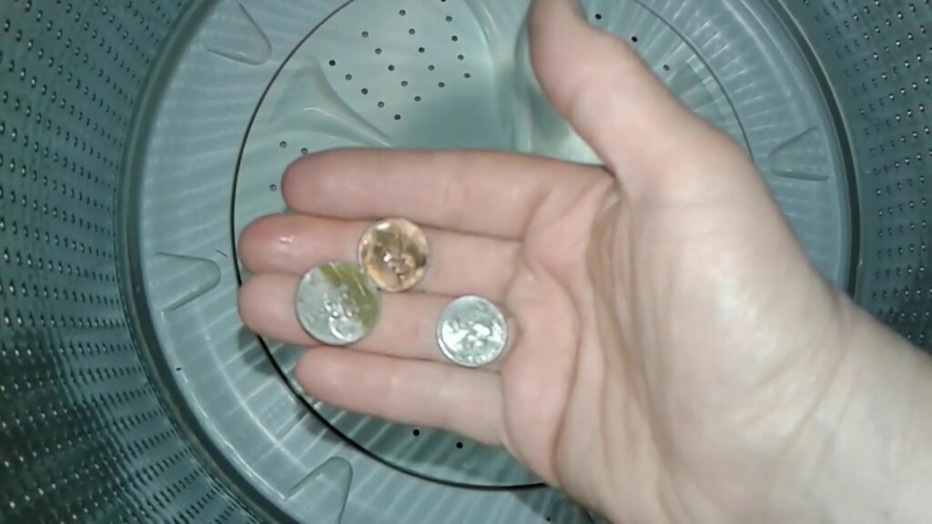 hand holding several coins inside what appears to be a top-load washing machine drum