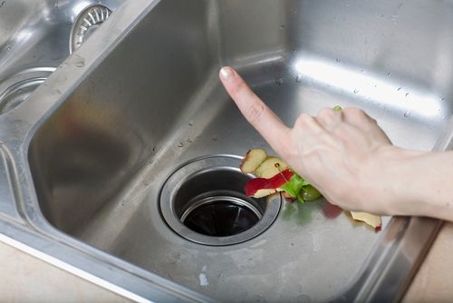 a person putting food scraps into a kitchen sink garbage disposal unit