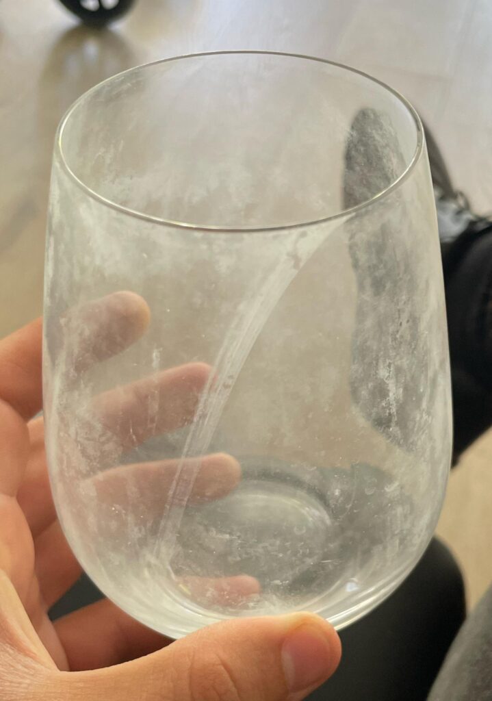 a clear, stemless wine glass covered in a cloudy film or white spots